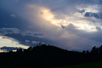 Kleine Kirche auf bewaldetem Hügel unter schweren dramatischen Gewitterwolken