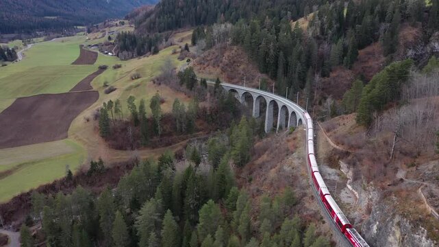 Aerial view of a red train crossing the majestic Landwasser Viaduct, a stone railway bridge amidst the forests, Berg&uuml;n Filisur, Grisons, Switzerland.