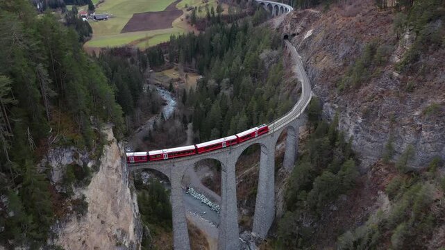 Aerial view of Landwasser Viaduct and train contrasting against the surrounding green forest and rocky terrain in the Swiss Alps, Berg&uuml;n Filisur, Grisons, Switzerland.