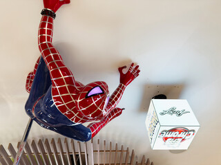Naklejka premium Spider Man statue clinging to a blue chair beside a white cube display in a bright room