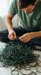 Man untangling a messy pile of tangled Christmas lights on the floor. Holiday preparation and decorating chores at home. Close-up of hands working on festive string lights