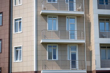 Obraz premium Apartment building facade with beige tiles and metal railings. Balcony detail for residential architecture or real estate marketing. Real photo