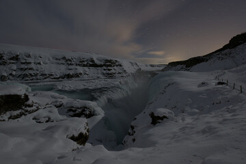 View of the majestic Gullfoss waterfall plunging into the gorge surrounded by snow-covered cliffs under a starlit sky, Gullfoss, Hrunamannahreppur, Iceland.