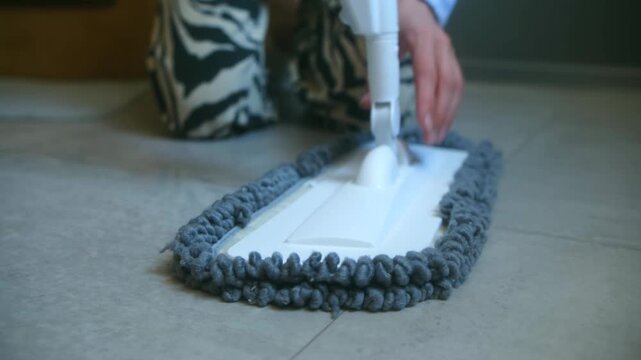 Close up person hands fitting gray chenille microfiber pad on white flat mop head, preparing cleaning equipment for mopping floor in modern home. Person attaching microfiber mop head to floor cleaner