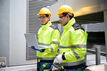 Engineer or workers in safety vests and helmets inspecting a laptop computer in industrial...