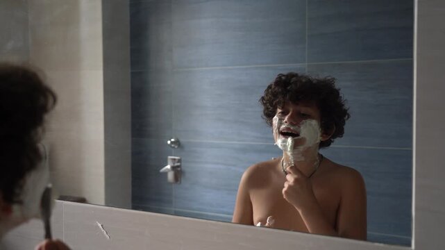 11-year-old boy playfully shaves his beard by putting his father's shaving cream in the bathroom at home - puberty and lifestyle  of a teenager - imitate   adult behavior , growth stages of children