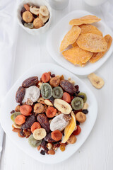 Mix of dried tropical fruits, nuts, and raisins on a white table.