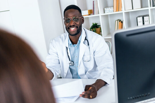 Cheerful gynecologist reviewing the medical history of her pregnant patient with computer in the clinic
