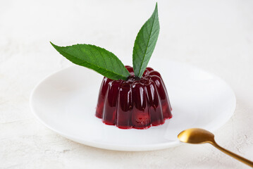 Jelly with cherry and green leaves in a plate with golden spoon. Vegan, sugar and lactose free.
