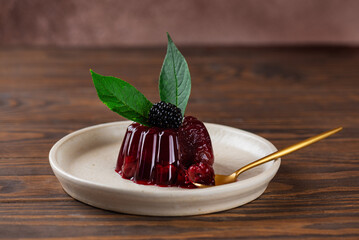 Berry jelly with fresh cherry, blackberry and green cherry leaves with golden spoon on brown wooden table. Healthy food, vegan, sugar, gelatin and lactose free.