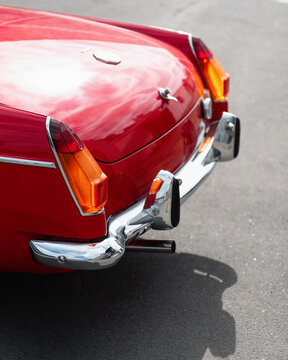 Rear of old red british car. 1960s MG MGB roadster with chrome bumper and big tail lights. Shiny bodywork reflecting sky on a sunny day. Kyiv, Ukraine - September 30 2024