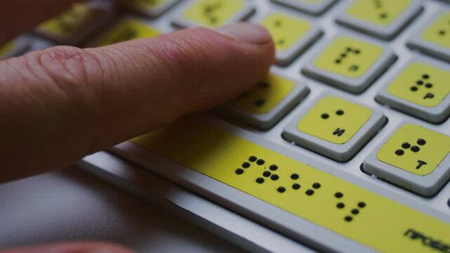 Computer keyboard with braille font alphabet. Blind person is typing words, hands. Technological device for visually impaired people. Tactilely touches bumps on keys. Inclusion, assistive technology