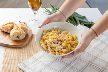 Hands serving pasta carbonara with bacon and cream