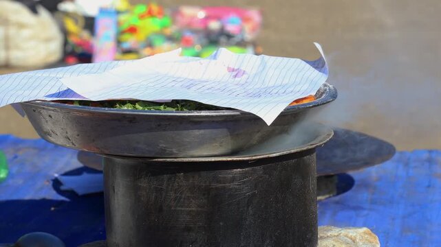Steam rises from a partially paper-covered pot in an outdoor rural setup, capturing traditional cooking practices, natural simplicity, and authentic countryside life.