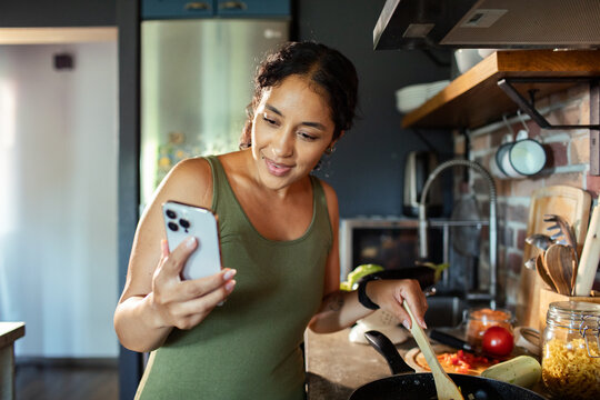 Woman cooking and using smartphone