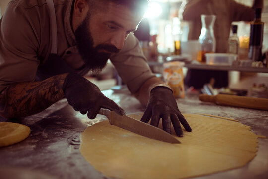 Adult male chef cutting dough in kitchen