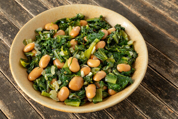 Italian chicory greens and white beans (Cicoria e Fagioli) in a bowl on wooden rustic background.