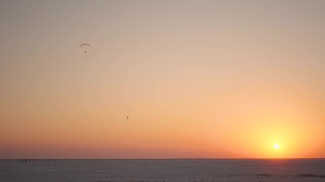4K shot of sunset at the Rann of Kutch during the winter season with people enjoying paragliding in the sky as seen from Kutch in Gujarat, India. Scenic view of sunset at White desert in Kutch region.