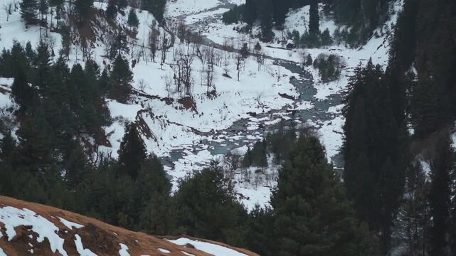 Slow motion shot of river stream surrounded by snow during the winter season as seen on the way towards Aru Valley in Pahalgam, Jammu and Kashmir, India. Scenic view of river in mountain valley. 