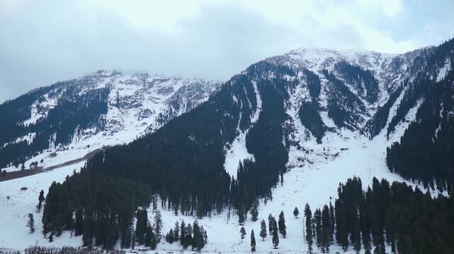 Wide angle shot of snowy Himalayan mountain range with dark clouds above it during the winter season as seen at Betaab Valley in Pahalgam, Jammu and Kashmir, India. Scenic snowy Himalayas in winter. 