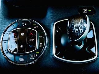 A close-up of a modern vehicle's center console featuring the circular automatic climate control panel with 'AUTO' and 'DUAL' zones, positioned next to a sleek electronic gear selector 
