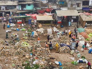 Dhaka, Bangladesh - 18 February 2025: Aerial view of a bustling market scene unfolds, vibrant with activity and piles of produce along the steps near the riverbank.