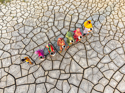 Gabura Union, Bangladesh - 25 April 2025: Aerial view of women walking across parched earth, their vibrant clothing a stark contrast to the cracked, arid landscape.