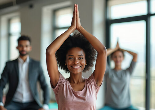 Diverse colleagues practice yoga poses indoors. A smiling woman leads a group meditation session in a bright office. Team building activity promotes workplace wellness and mental health.