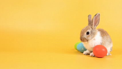 Süßes Babykaninchen mit bunten Ostereiern auf gelbem Hintergrund
