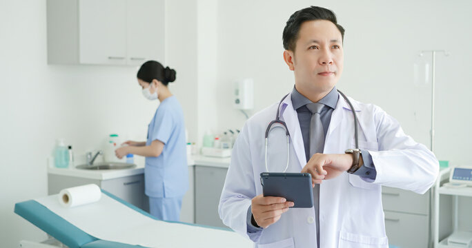 Portrait of asian senior doctor standing  while using tablet and checking time of appointment.