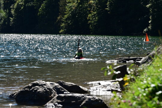 Kleines M&auml;dchen im Neoprenanzug von hinten in einem Bergsee, Im Hintergrund ein kleines Segelboot