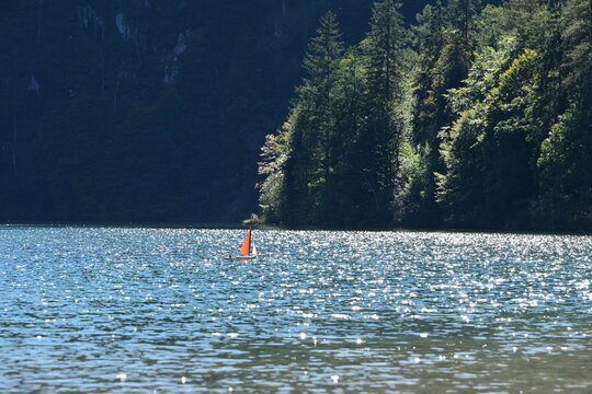 Kleines Modelsegelschiff mit orangen Segeln auf einen Bergsee