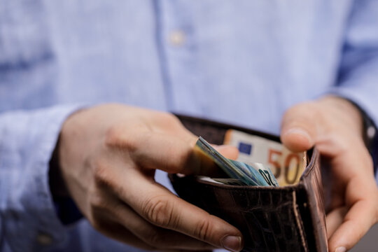 Close-up shot of a man's hands opening a leather wallet filled with euro banknotes, symbolizing financial concepts and economic activity.