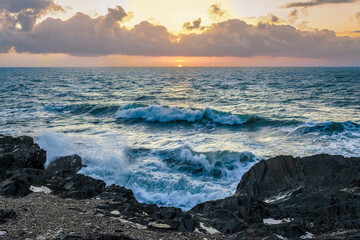 Golden sunrise over the Irish coast, waves crashing on dark rocks, dramatic sky with warm light reflection.