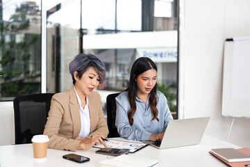  Teamwork process. Two Asian businesswoman working pointing laptop computer and discussing...