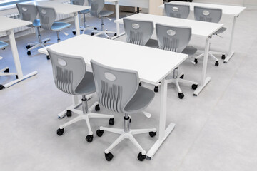 Modern classroom with white tables and gray rolling chairs on light floor. Educational furniture for school or training environment. Real photo