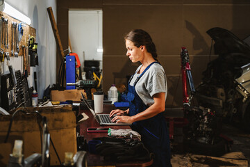 Female worker using laptop in local auto repair shop.