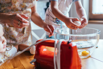 Little boy cracking eggs into bowl while mother helps with breakfast