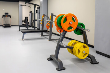 Obraz premium Gym interior with weight rack holding colorful plates and barbells. Fitness equipment for strength training or bodybuilding. Real photo
