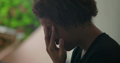 Young boy in emotional distress, hands covering face, crying, standing against wall, African...
