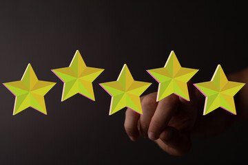 Hand reaching out to glowing five stars. Represents rating, feedback, review, or quality assurance,...
