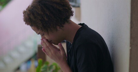 Young boy in emotional distress, sitting with head lowered, hands covering face, African descent, feeling overwhelmed, outdoor setting