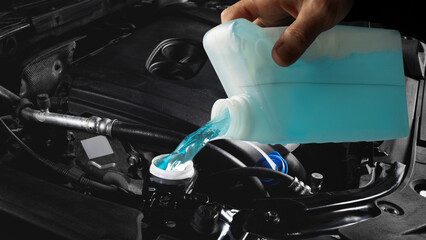 Mechanic pouring blue washer fluid into car engine compartment macro view. Concept of automotive maintenance, fluid efficiency, and service training materials for technical education visuals.