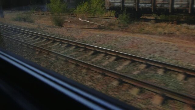 View from A moving train showing parallel railway tracks. A Concrete platform with graffiti and freight cars pass by. Sunny day journey on a railroad.