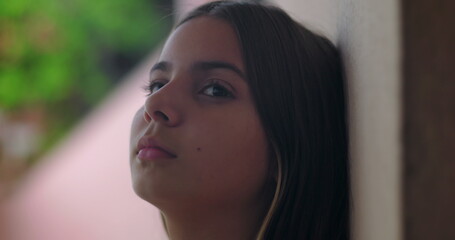 Young girl with brown hair closing eyes, leaning against wall outdoors, calm relaxed facial...
