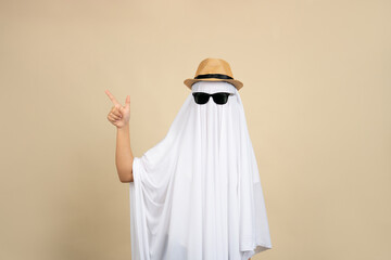 A woman in a Halloween ghost costume and hat points at something on a beige background.