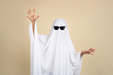 Halloween concept, white ghost wearing black glasses made of bedsheets on beige background.