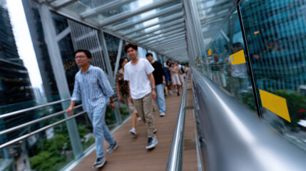 A bustling crowd of diverse individuals moves along a modern glass skybridge, bridging urban landscapes in a dynamic blend of city life and architectural innovation.