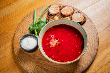 Rich red borscht with garlic bread and sour cream served on a wooden tray, cozy vibe