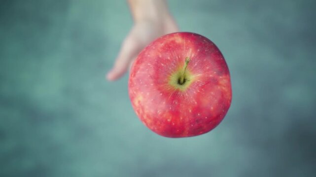 Hand holding a vibrant red apple against a blurred, textured blue-green background.